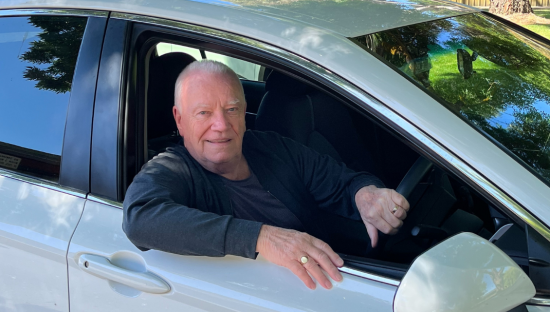 Image of a male driver in a silver car holding onto the car wheel.